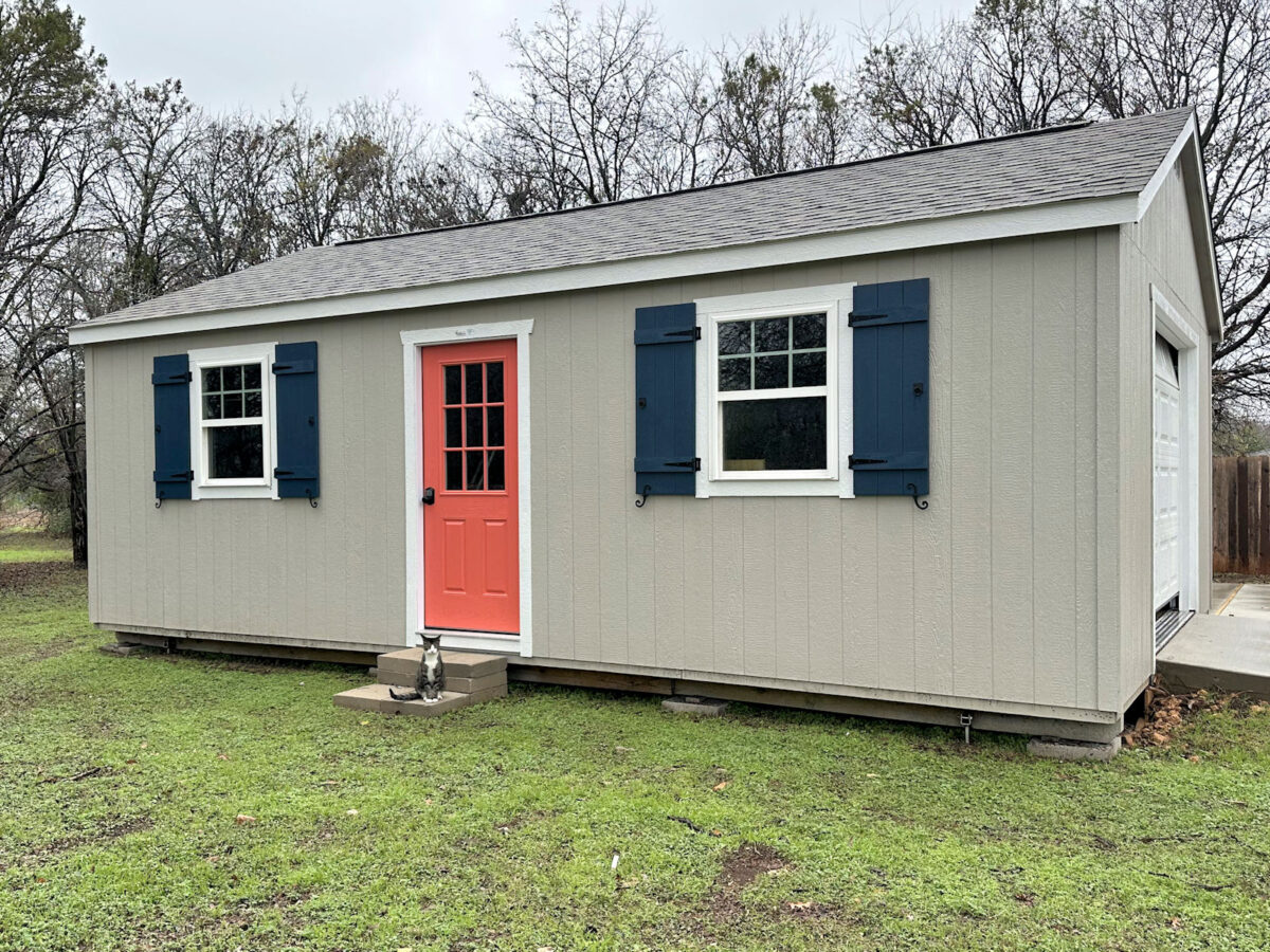 Back yard shed before skirting was added -- gray siding, white trim, navy blue shutters, coral front door